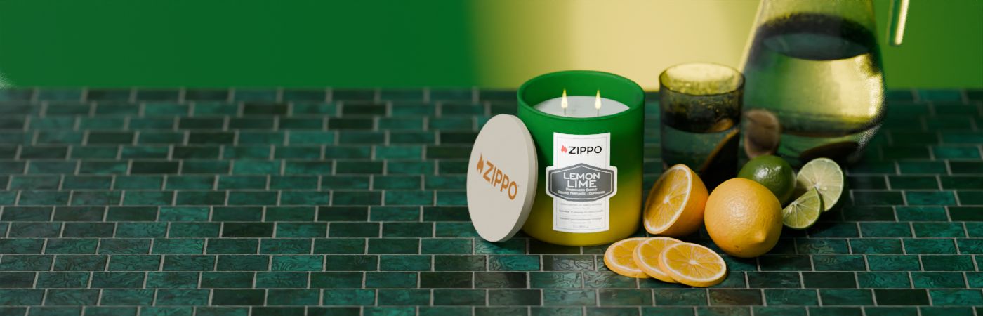 Eine grüne Zippo-Zitronen-Limetten-Kerze brennt auf einem dunkelgrünen Fliesentisch neben aufgeschnittenen Zitrusfrüchten und einer Karaffe, mit abgenommenem Deckel daneben.