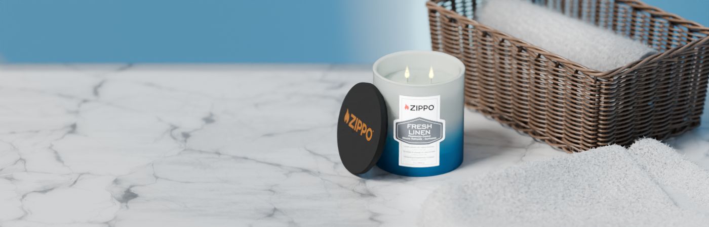 Eine Zippo-Kerze mit der Aufschrift „FRESH LINEN“ brennt auf einem Marmortisch neben gefalteten Handtüchern und einem Korb.