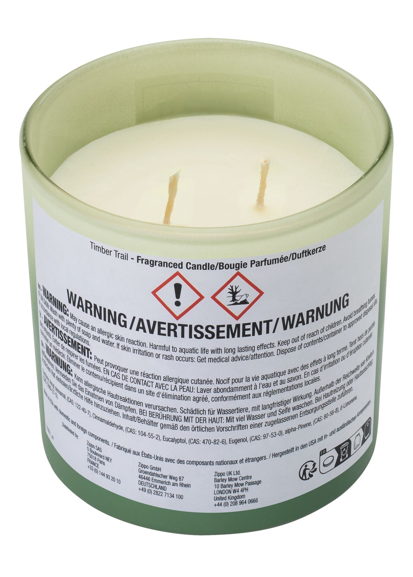 Eine Zippo-Duftkerze mit zwei Dochten befindet sich in einem grünen Glas mit einem Warnhinweis-Etikett; darin stehen: "WARNING/AVERTISSEMENT/WARNUNG," und Hinweise zu allergischen Hautreaktionen sowie Risiken für Wasserlebewesen.