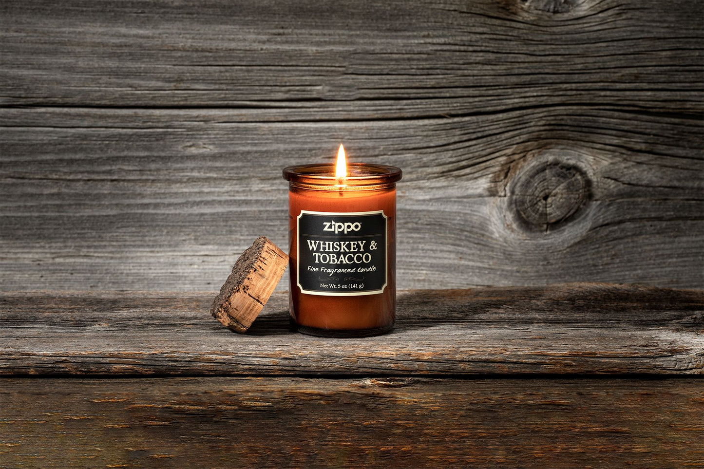 Zippo Kerze Whiskey und Tobacco braun mit Deckel aus Kork mit Flamme vor Holzhintergrund